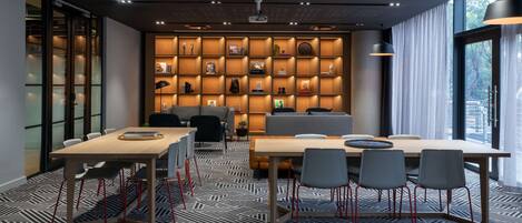 A modern meeting room with a large table, chairs, a sofa, and a bookshelf filled with books and decorative items.