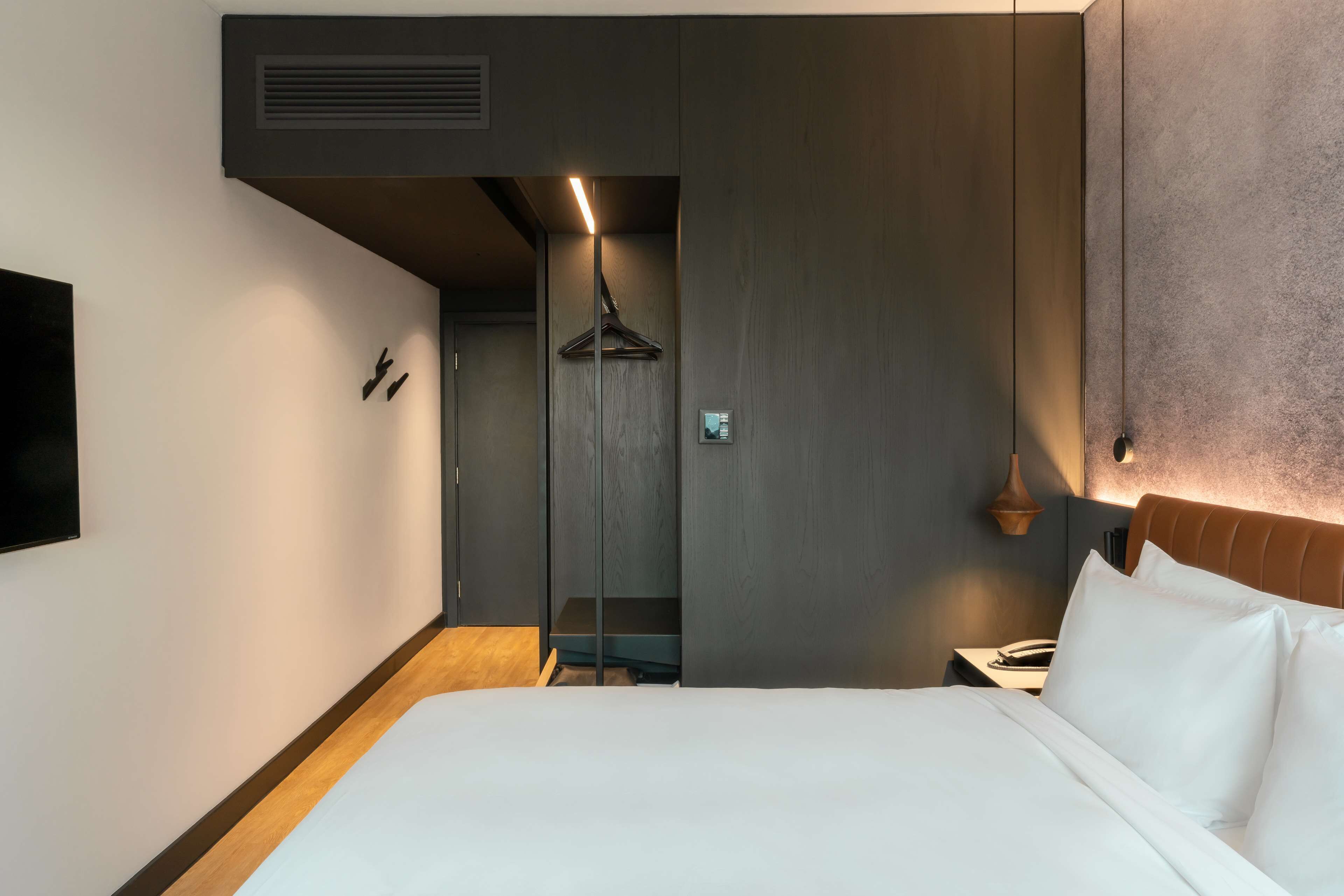 A modern hotel room with a bed, bedside table, and a hanging coat rack.