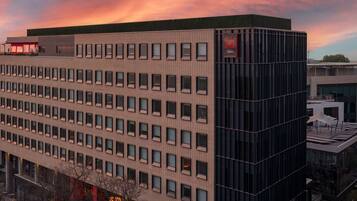 Un edificio moderno con una fachada de ventanas en forma de cuadrícula, un llamativo letrero que dice 'RED' y vista del cielo al atardecer.