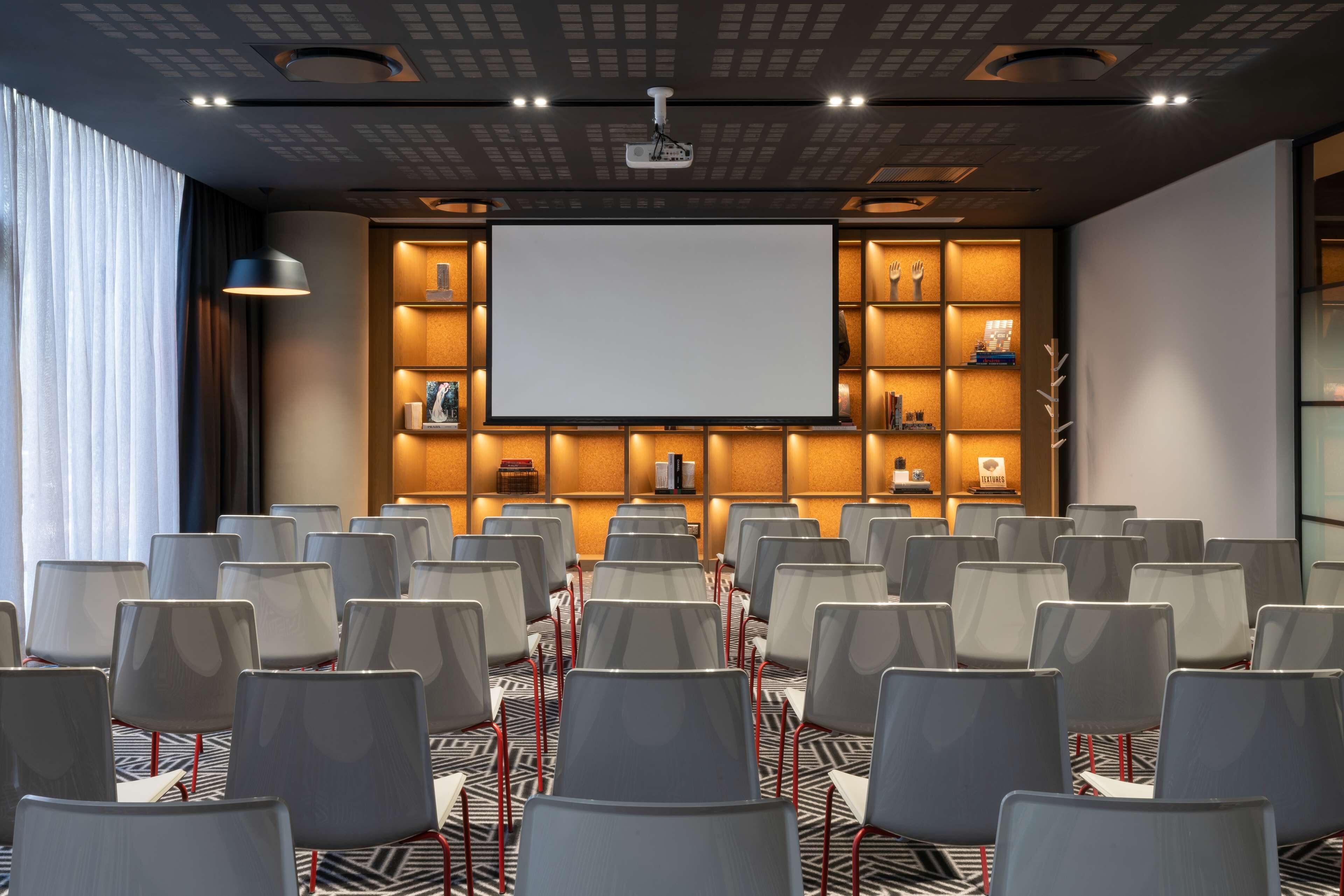 A conference room with rows of chairs, a large screen, and shelves with various items.