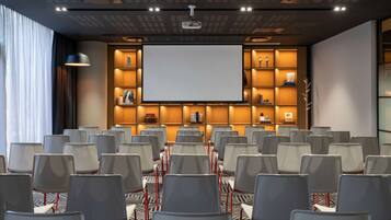 A conference room with rows of chairs, a large screen, and shelves with various items.