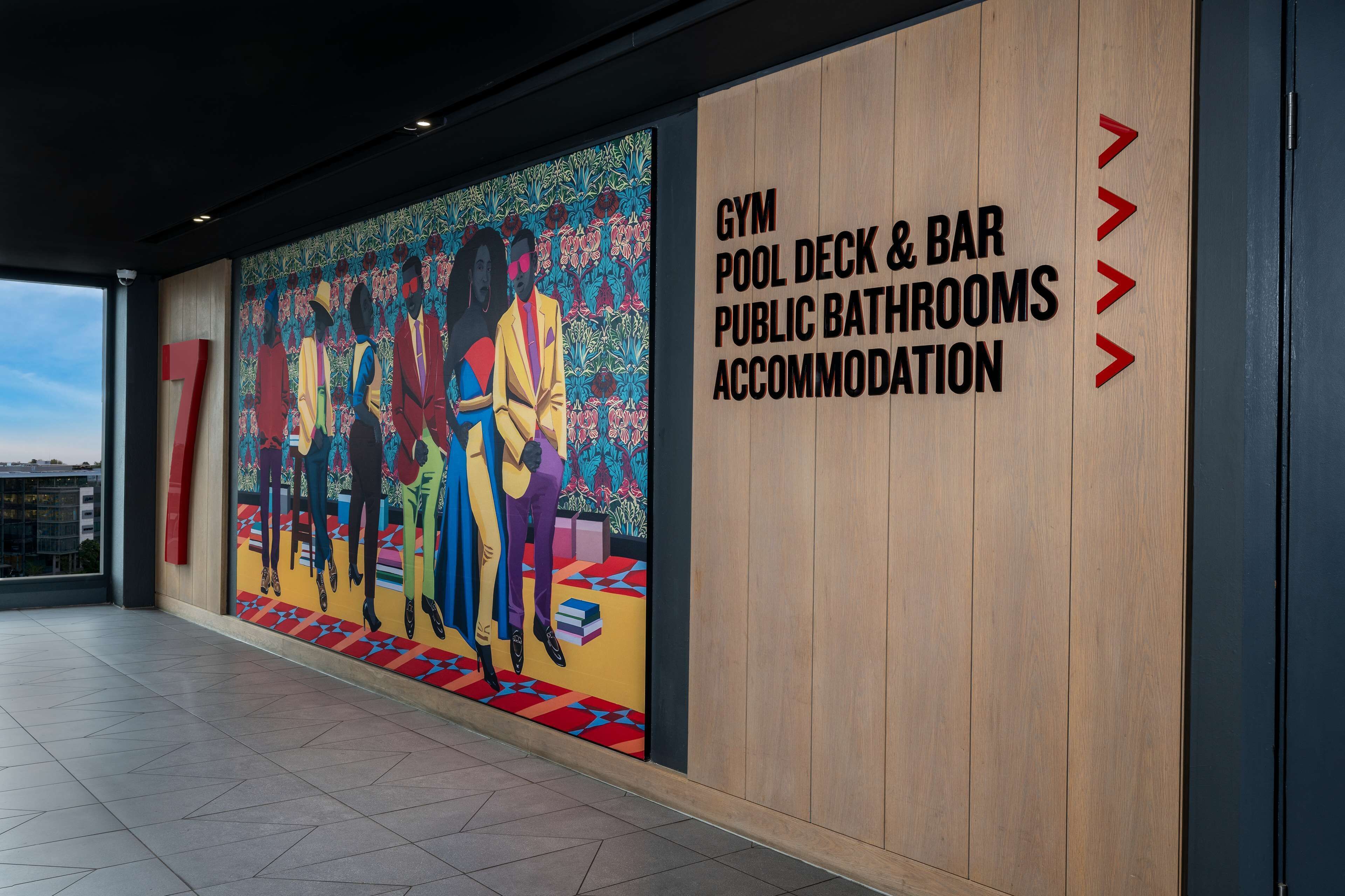 Una pared con un mural colorido y texto que indica servicios como gimnasio, terraza de piscina, bar, baños públicos y alojamiento.