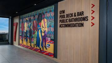 Una pared con un mural colorido y texto que indica servicios como gimnasio, terraza de piscina, bar, baños públicos y alojamiento.