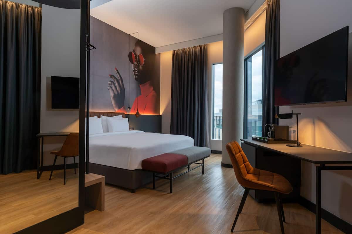 Una habitación de hotel moderna con una cama grande, un escritorio, una silla y un televisor.