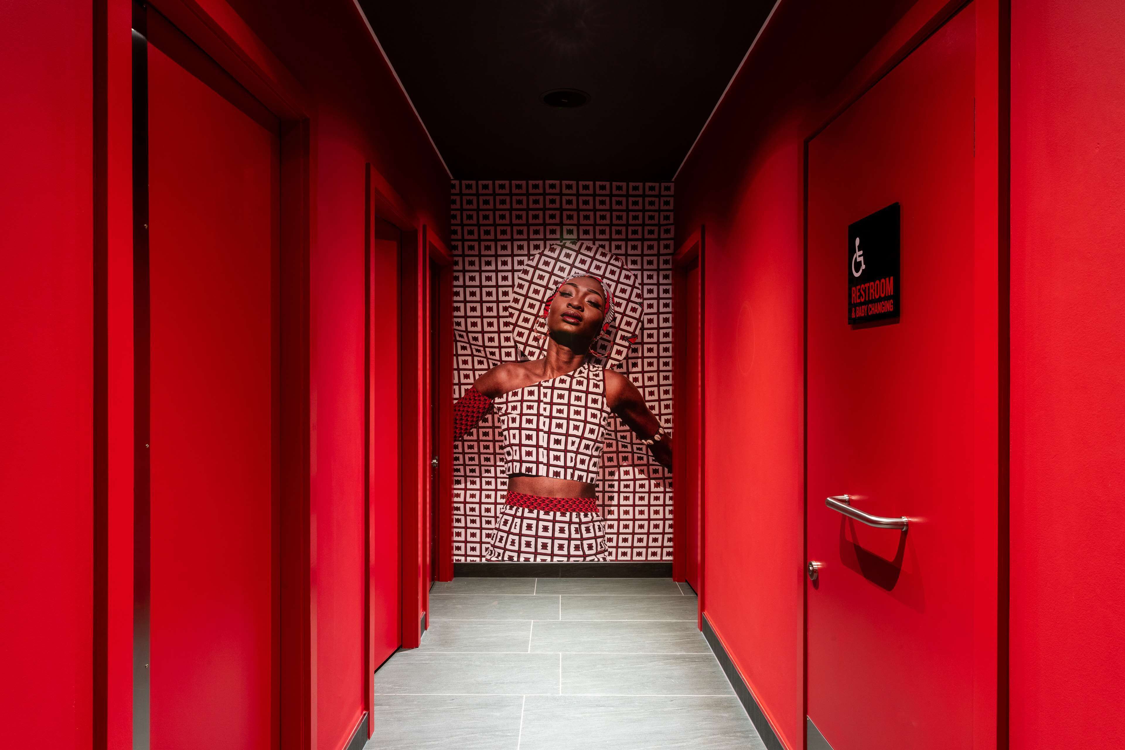 Un passadís vermell amb un senyal que indica un lavabans accessible i una sala per canviar el bolquers.