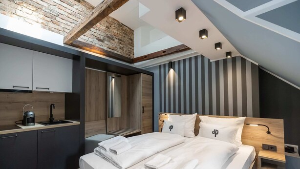 A modern hotel room with a lofted kitchen, a large bed with white linens, and a striped wall design. - Oldtown Studios by dasPaul (Nuremberg)
