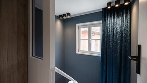 A staircase with a wooden handrail, a dark blue wall, a window with white trim, and a black door with a handle. - Oldtown Studios by dasPaul (Nuremberg)