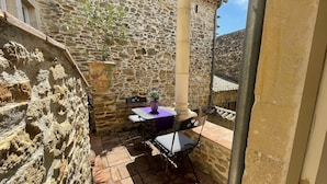 Un bâtiment en pierre doté d’une terrasse carrelée, d’une table avec des chaises et d’une plante en pot.