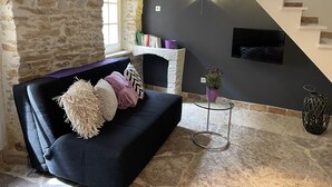 Un salon avec un mur en pierre, une cheminée, un escalier et un téléviseur fixé au mur.