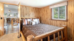 Une chambre aux murs lambrissés, comprenant un lit, une fenêtre et une porte donnant sur un coin repas.