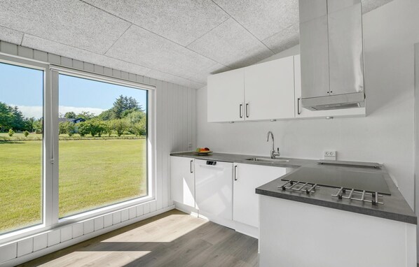 A modern kitchen with white cabinets, a stainless steel range hood, and a large window offering a view of a grassy yard.