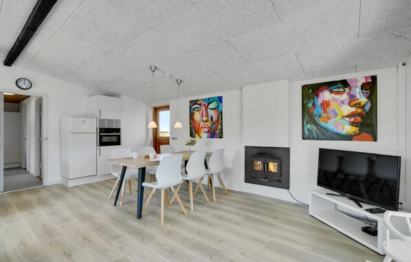Ein modernes Wohnzimmer mit Essbereich, weißen Wänden, einem Kamin und zwei großen Bildern.