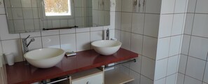 Une salle de bain avec deux lavabos blancs, un plan de toilette rouge, un miroir et une fenêtre.