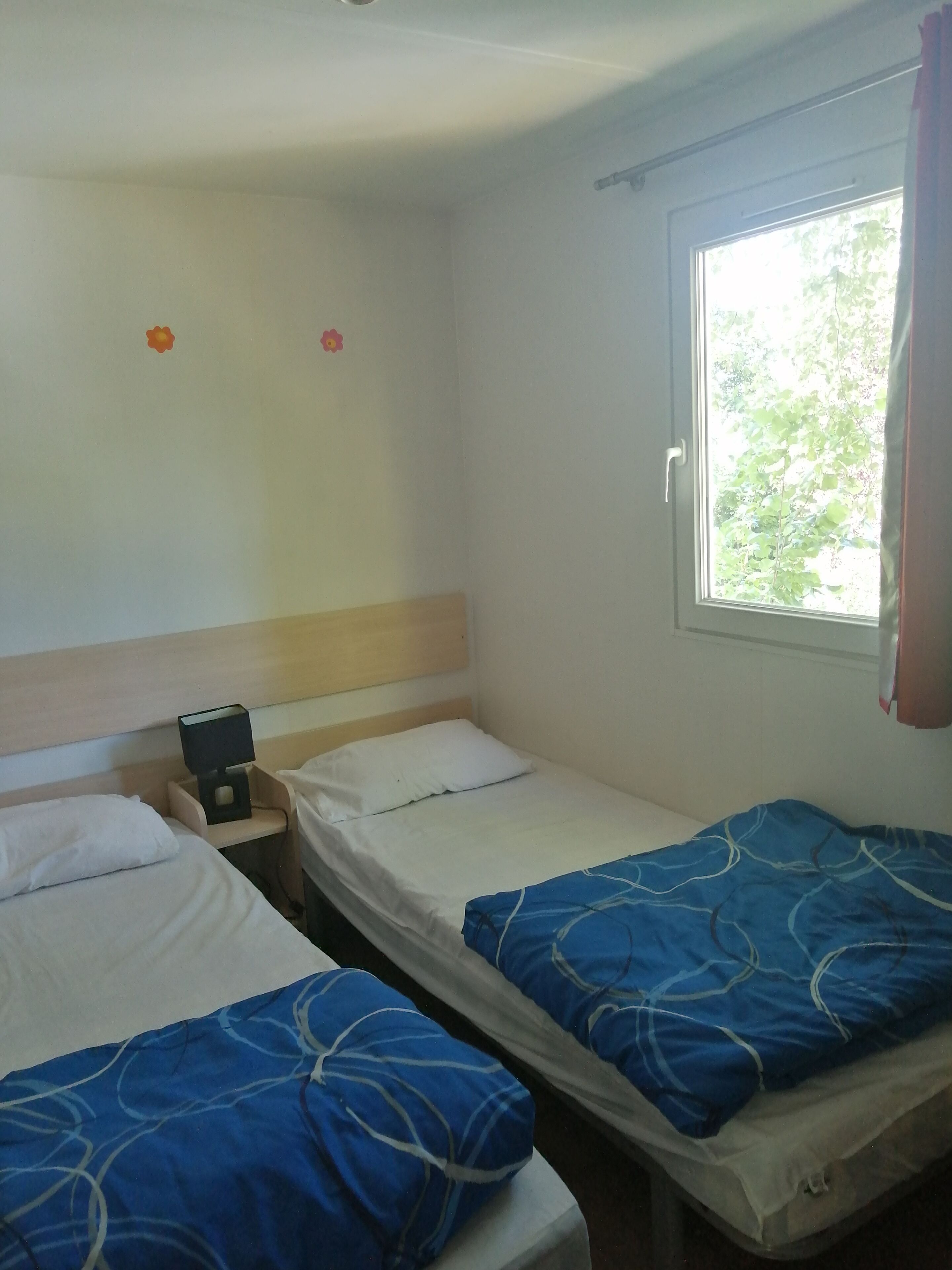 A room with two beds, a nightstand with a lamp, and a window with curtains.