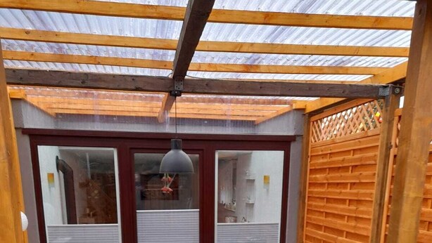 Un patio cubierto con una mesa y sillas, una puerta que da a una habitación y una cerca de madera.