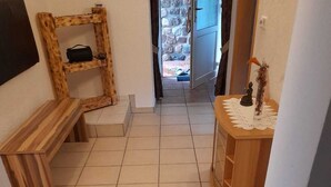 Un pasillo con suelo de baldosas, un banco de madera, una pequeña mesa con un objeto decorativo y una pared de piedra al fondo.
