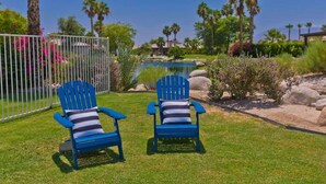 Deux chaises Adirondack bleues, dotées de coussins à rayures, se trouvent dans un jardin bien entretenu, agrémenté d’une piscine et de palmiers.