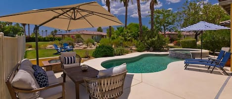 A backyard with a pool, lounge chairs, a table, and umbrellas.