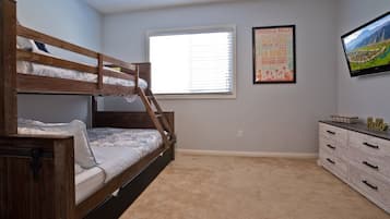 Cozy retreat with a bunk bed and single bed, a dresser, and a television.