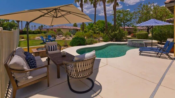 Un jardin avec une piscine, des chaises longues et une table placée sous un grand parasol.