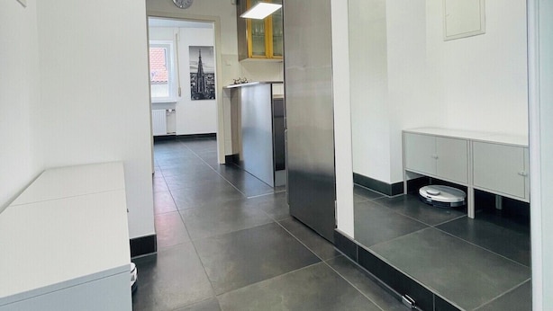 A modern hallway with a clean, minimalist design, featuring a stainless steel refrigerator, a mirror, and a small trash bin. - Superior 3 room Apartment Cathedral View (Ulm)