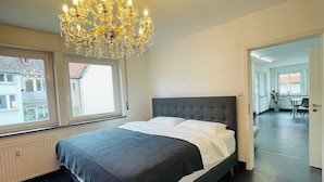 A bedroom with a large bed, a chandelier, and a view through a window. - Superior 3 room Apartment Cathedral View (Ulm)