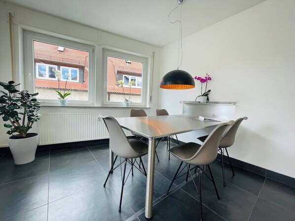 Un comedor con mesa y sillas, una planta en maceta y una ventana con vistas a edificios.