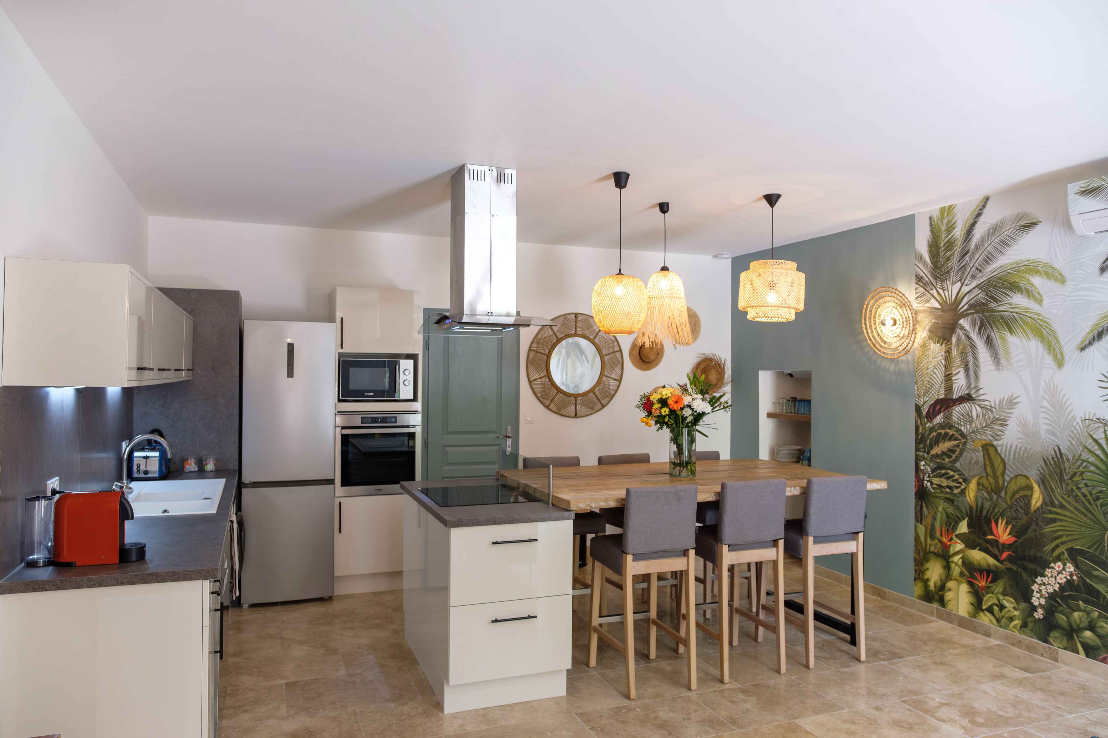 Une cuisine moderne avec un coin repas, comprenant un îlot central, des appareils électroménagers intégrés et une fresque murale aux motifs tropicaux.
