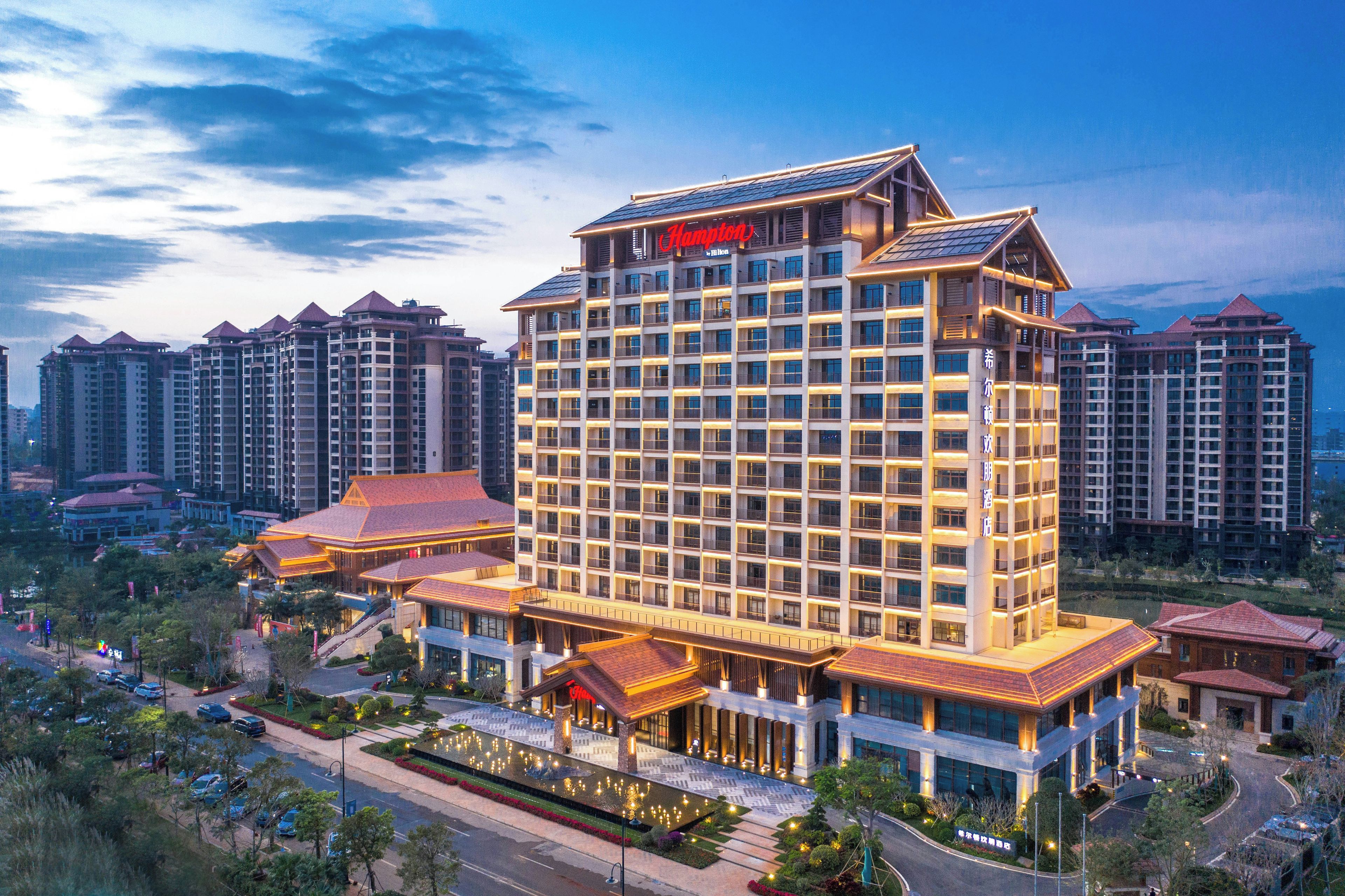 A multi-story hotel with a prominent 'Hampton' sign, surrounded by high-rise buildings.
