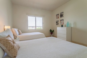 A bedroom with two beds, a window, a dresser, and wall decorations. - Pool Access! 2BR Condo w Balcony near Eagle Beach (Eagle Beach)