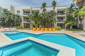 A hotel with a swimming pool, palm trees, and a multi-story building. - 2BR Condo w/ Balcony & Pool near Eagle Beach (Eagle Beach)