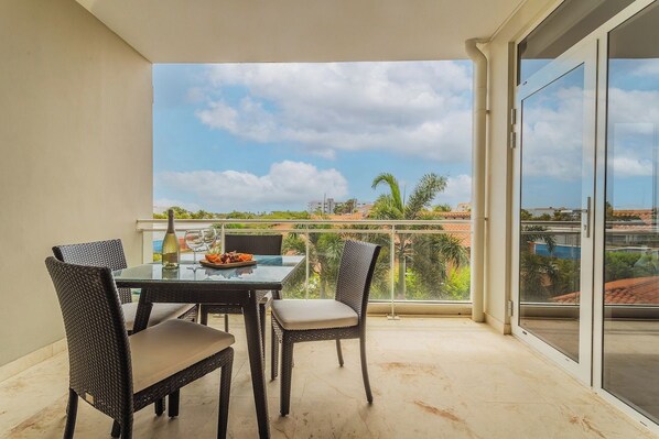 Un balcón con puerta de cristal, una mesa de comedor con sillas y vistas a la ciudad.