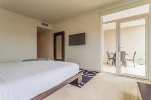 Une chambre d’hôtel comprenant un lit, une télévision et une porte-fenêtre coulissante donnant sur un espace extérieur avec une table et des chaises.