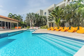 A swimming pool with lounge chairs and a building with balconies. - Pool Access! 2BR Condo w Balcony near Eagle Beach (Eagle Beach)