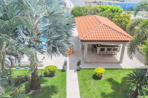 A covered outdoor seating area with a tiled roof, surrounded by well-maintained grass and palm trees. - Pool Access! 2BR Condo w Balcony near Eagle Beach (Eagle Beach)