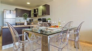 Een moderne keuken met een glazen eettafel, transparante stoelen en roestvrijstalen apparatuur.