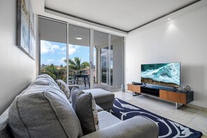 Un salon moderne comprenant un canapé, un téléviseur à écran plat et une porte-fenêtre coulissante donnant sur un espace extérieur.