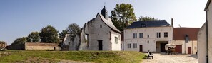 Um edifício histórico com fachada branca e telhado preto, um prédio grande e branco com várias janelas, e uma carroça coberta em frente.
