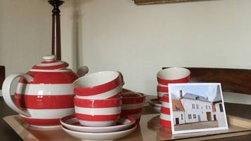 Une table mise avec une théière, des tasses et des soucoupes à rayures rouges et blanches, une lampe et un tableau représentant une maison.