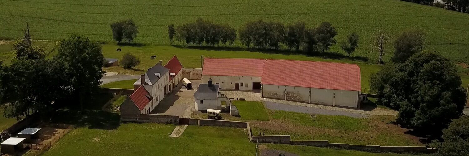 A rural farmstead with multiple buildings, including a large barn and several smaller structures, surrounded by expansive green fields.