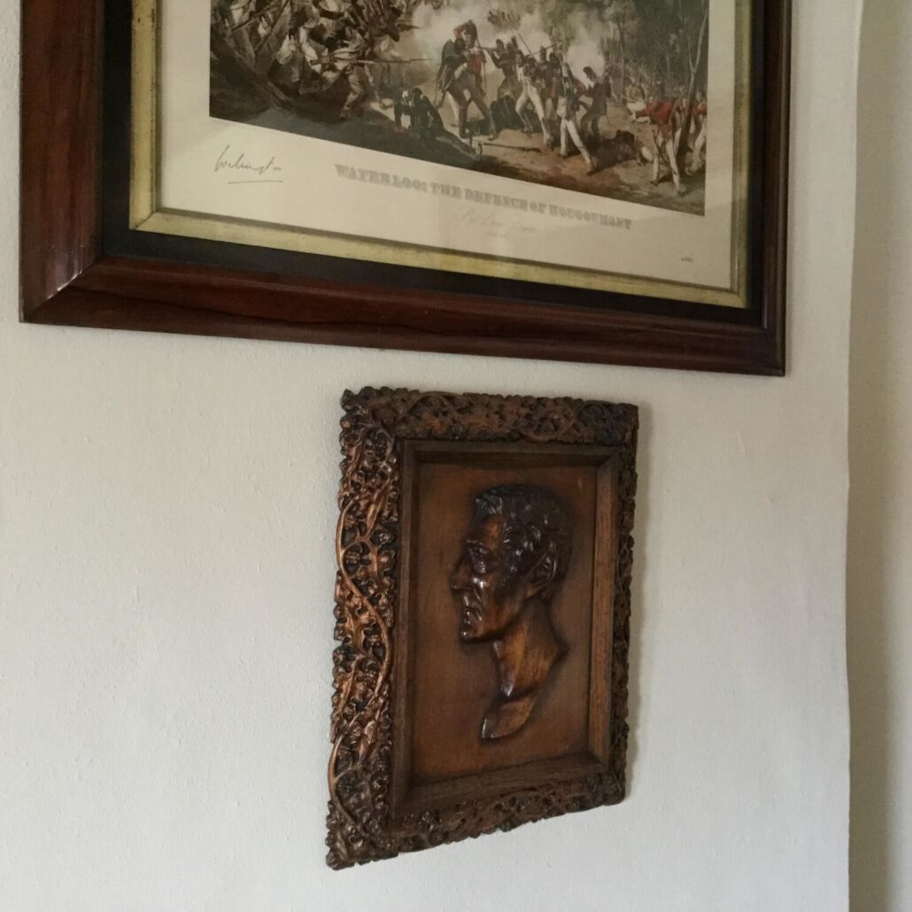 Ein gerahmtes historisches Gemälde und eine Holzskulptur an einer Wand.