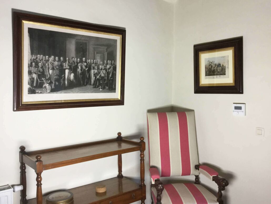 Um quarto com uma fotografia a preto e branco emoldurada, uma poltrona riscada e uma mesa de cabeceira de madeira.