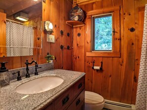 Baño de cabaña de madera con lavabo de granito, ventana y ventilador.