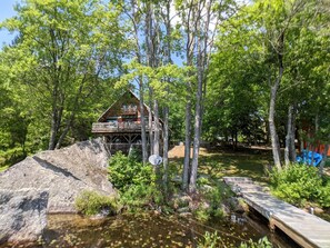 A cabin with a deck, surrounded by trees and a small stream.