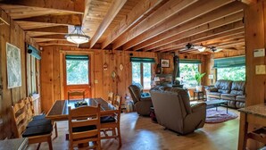 A wooden cabin interior with a dining table, chairs, a sofa, and a fireplace. - Lakes End Log Cabin on Lake Wicwas! (Meredith)