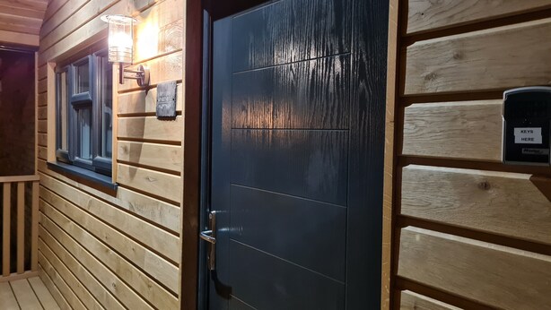 Eine Holzfassade mit einer dunklen Tür, einem Fenster und einem Briefkasten.