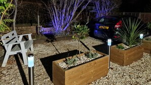 Ein Garten mit Holzpflanzgefäßen, einer Bank und einem in der Nähe stehenden Auto.