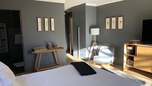 A hotel room with a bed, a desk with a lamp, a chair, and a TV on a wooden cabinet.