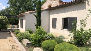A house with a stone facade, a tiled roof, and a garden with various plants and a lawn.