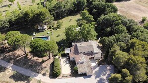 An aerial view of a property with a swimming pool, a patio area, and a house surrounded by trees.